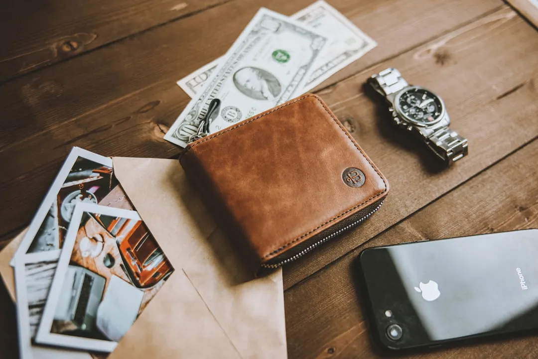 A wallet on a wooden table next to a cell phone
