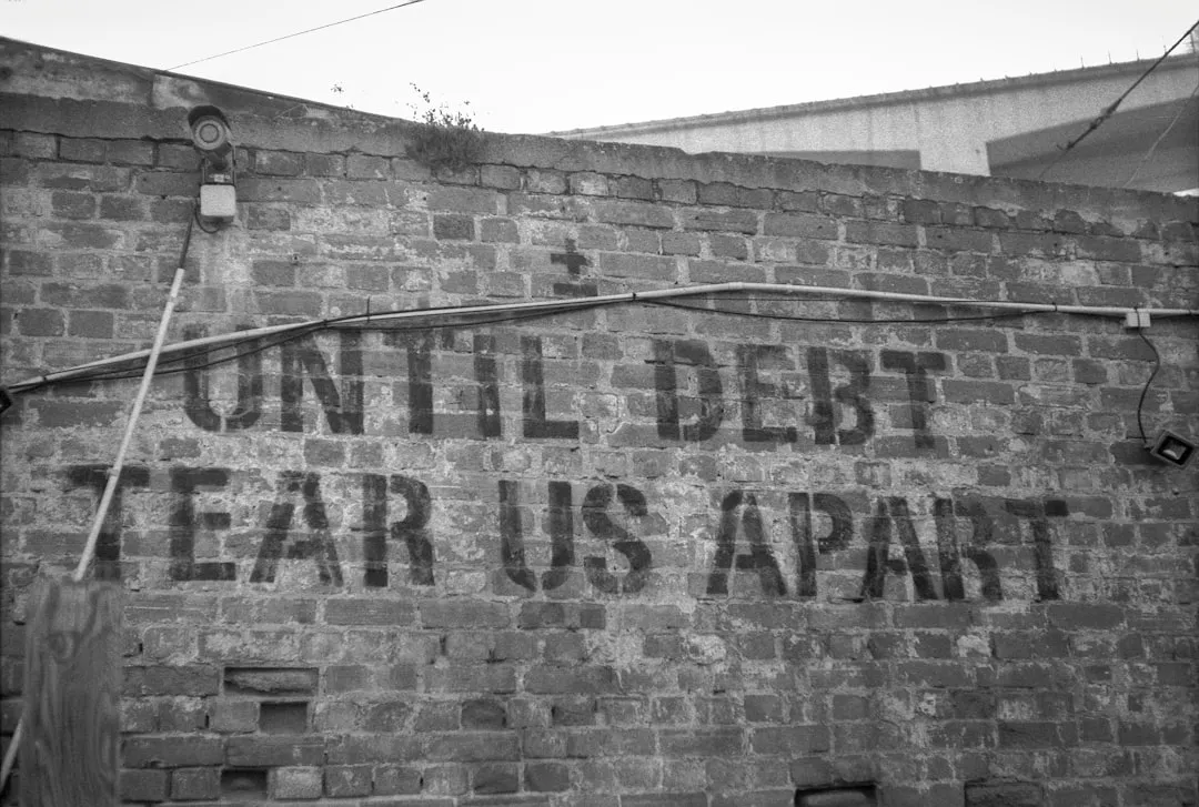 A sign on a brick wall that reads until debt tears apart
