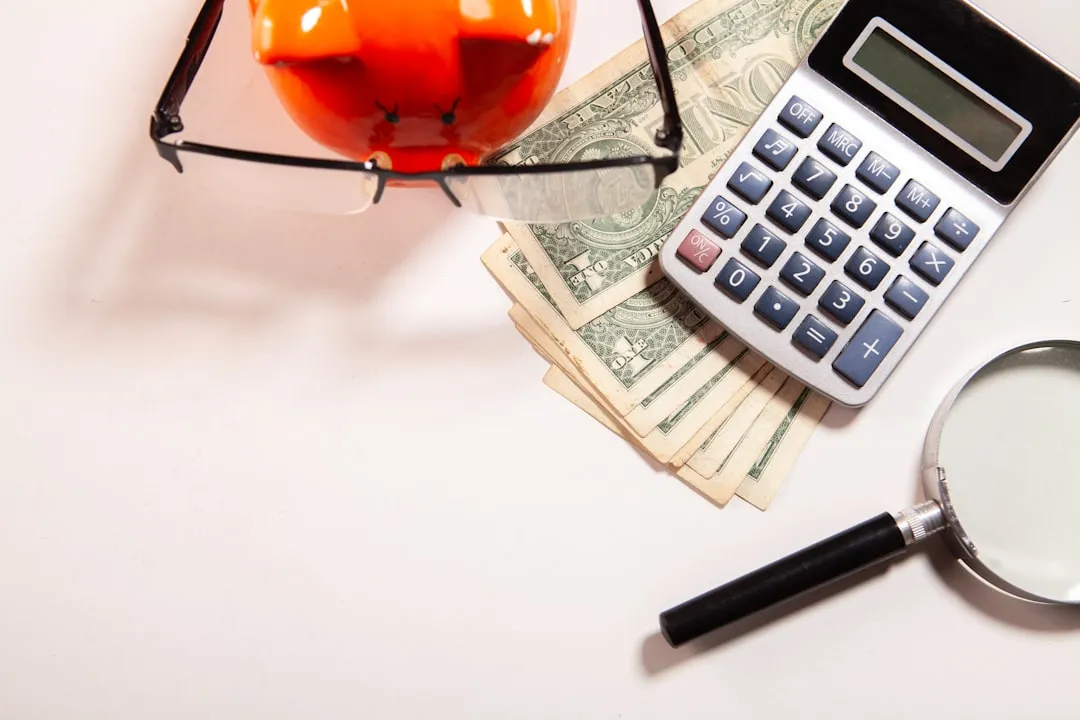 Calculator, magnifying glass, glasses, and money on a white surface.